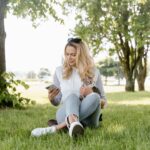 a woman sitting on the grass while using her phone and holding her cat